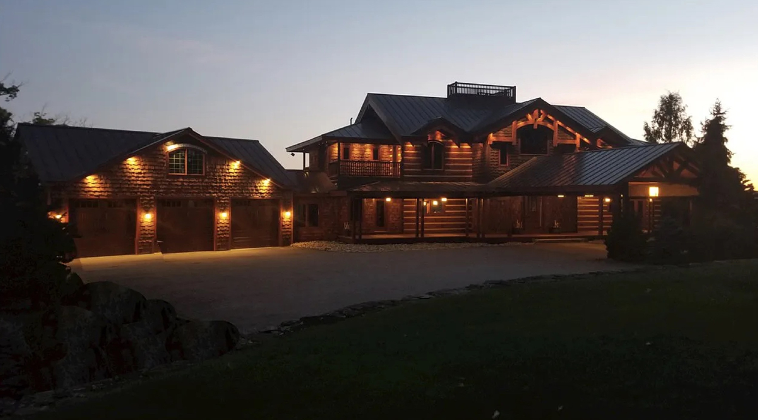 A finished custom Merrimac log home at dusk with lights glowing from the windows
