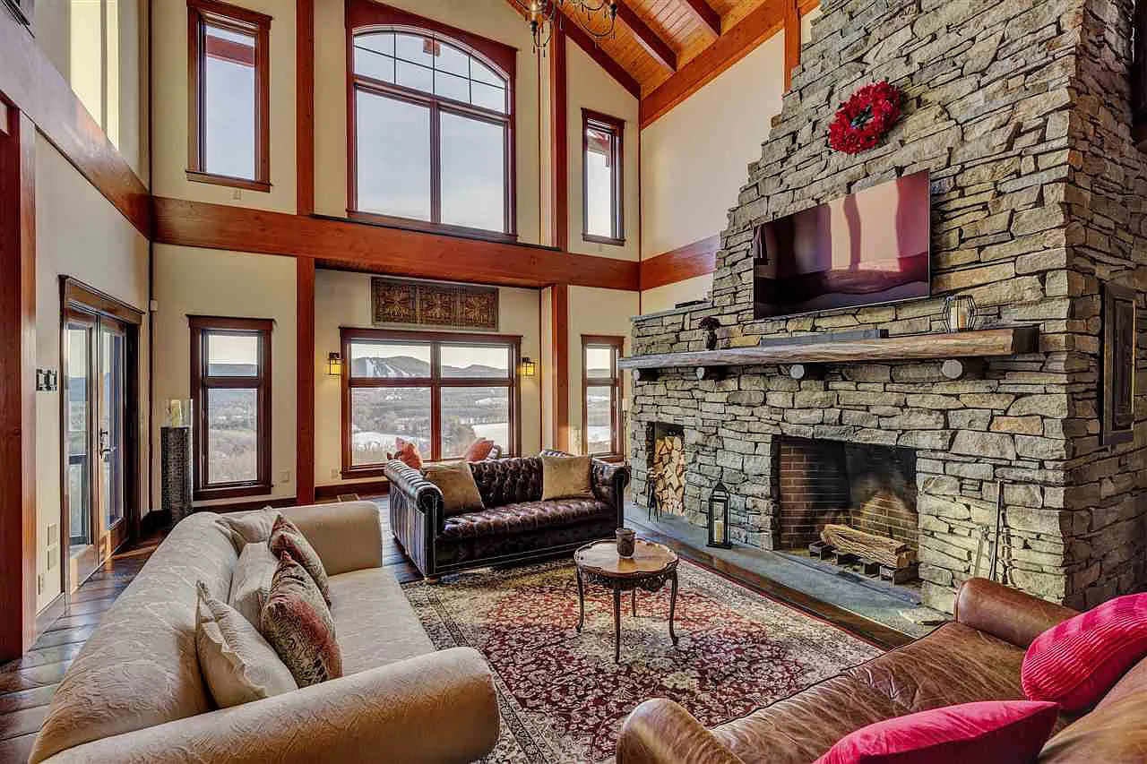 A finished log home interior at dusk with a cathedral ceiling, stone fireplace, leather furnishings, and warm interior lighting