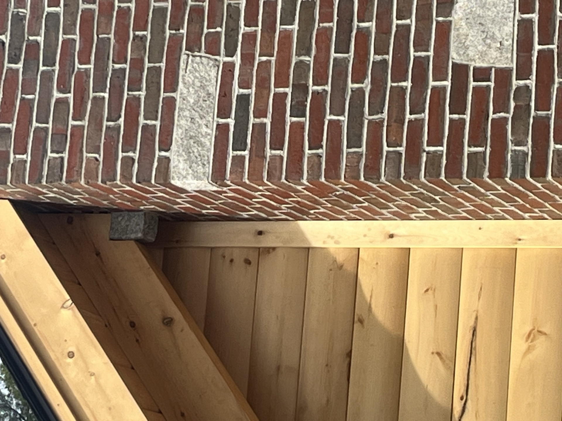 Close-up detail of the brick chimney capstone meeting the pine ceiling soffit