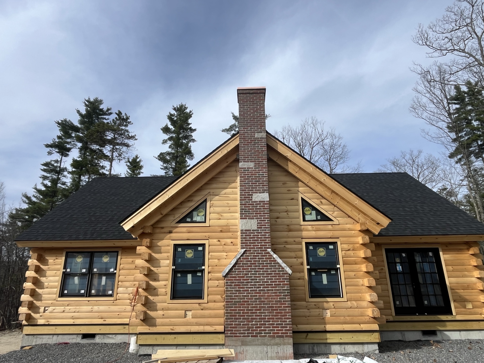 The Little Sunapee under construction in the mountains of New Hampshire, showing the central brick chimney, triangular gable windows, and two-wing log home layout