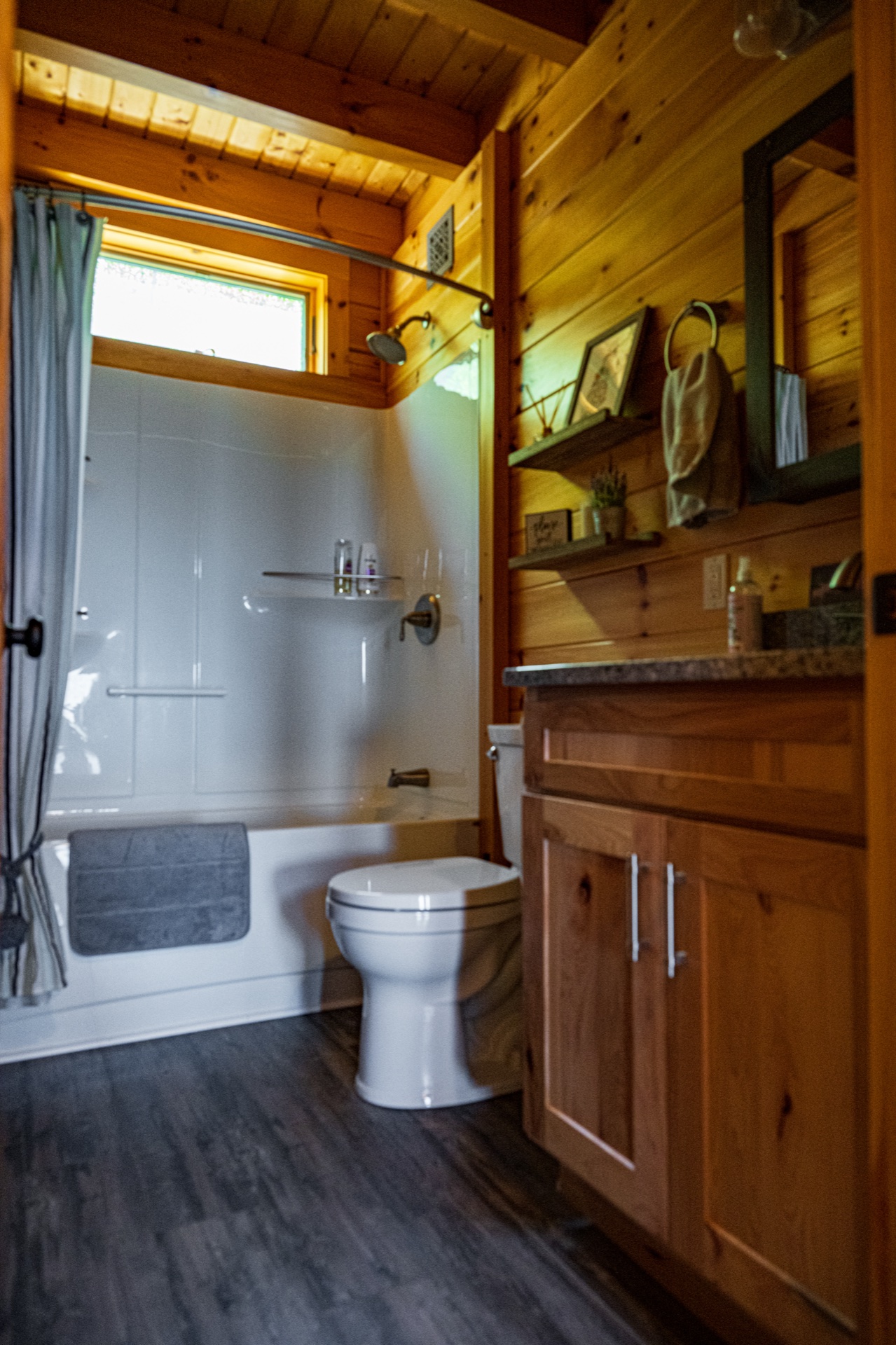 Ossipee bathroom with tub-shower combo, warm wood walls, window, and hickory vanity
