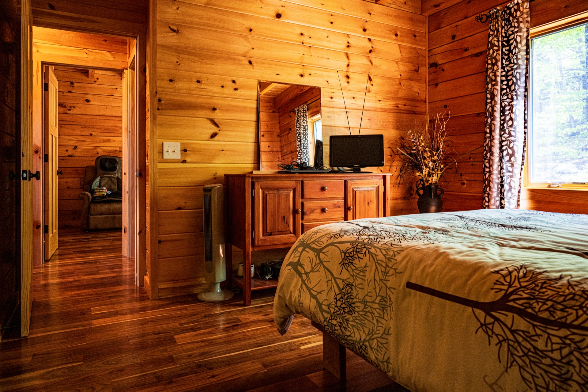 Ossipee bedroom with branch-pattern quilted bedding, dresser, TV, and warm log walls