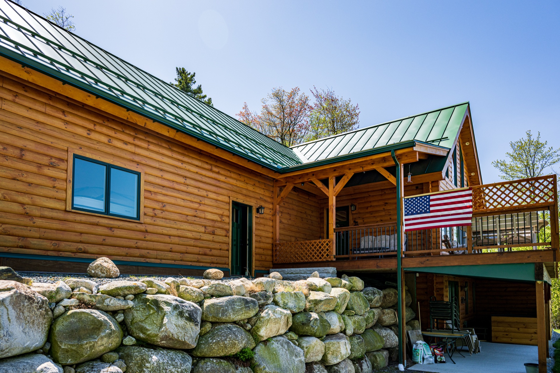 The Ossipee log home with American flag hanging from the deck, dry-stack stone retaining wall