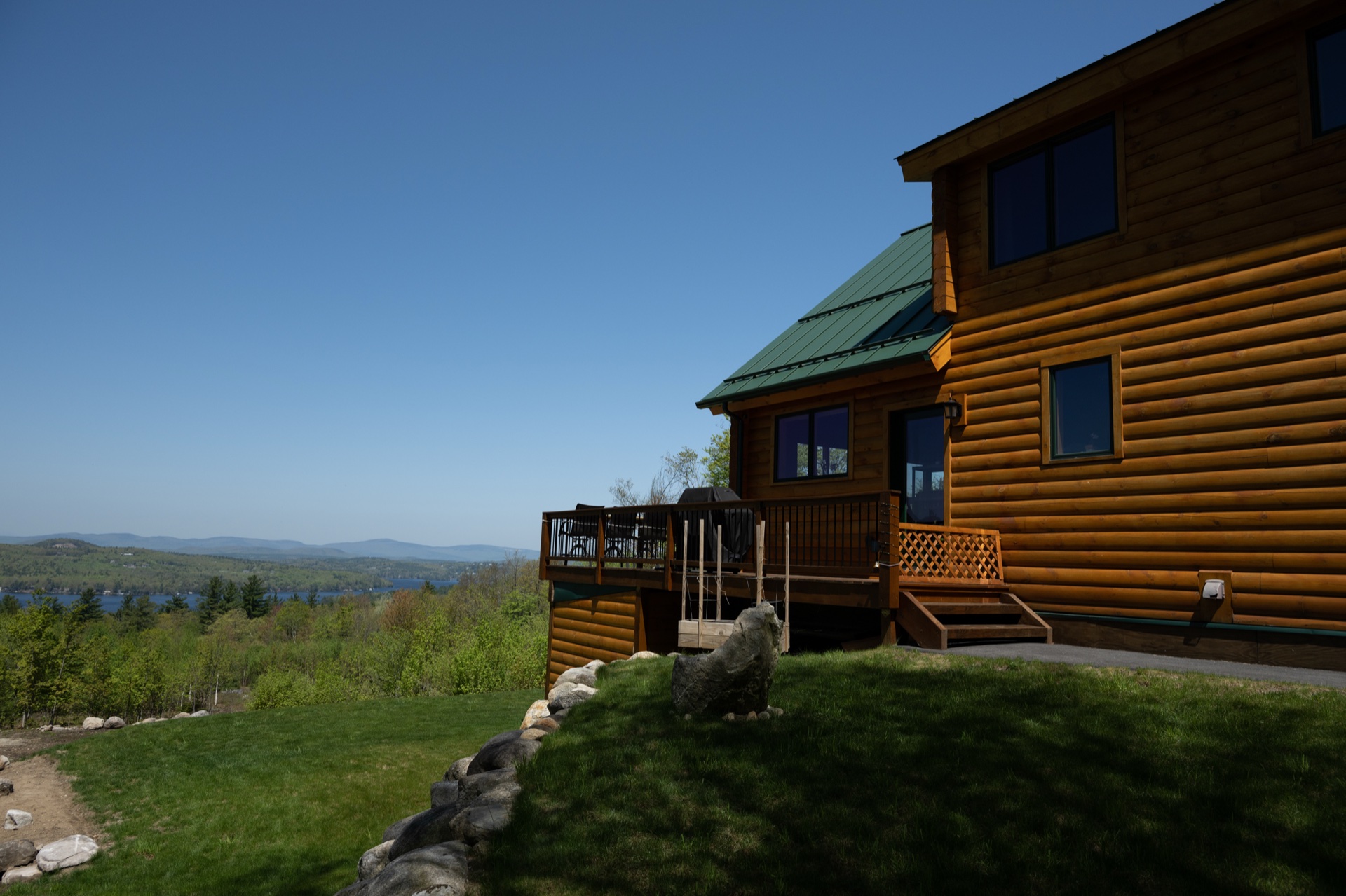 The Ossipee log home with green metal roof and lake view in the distance