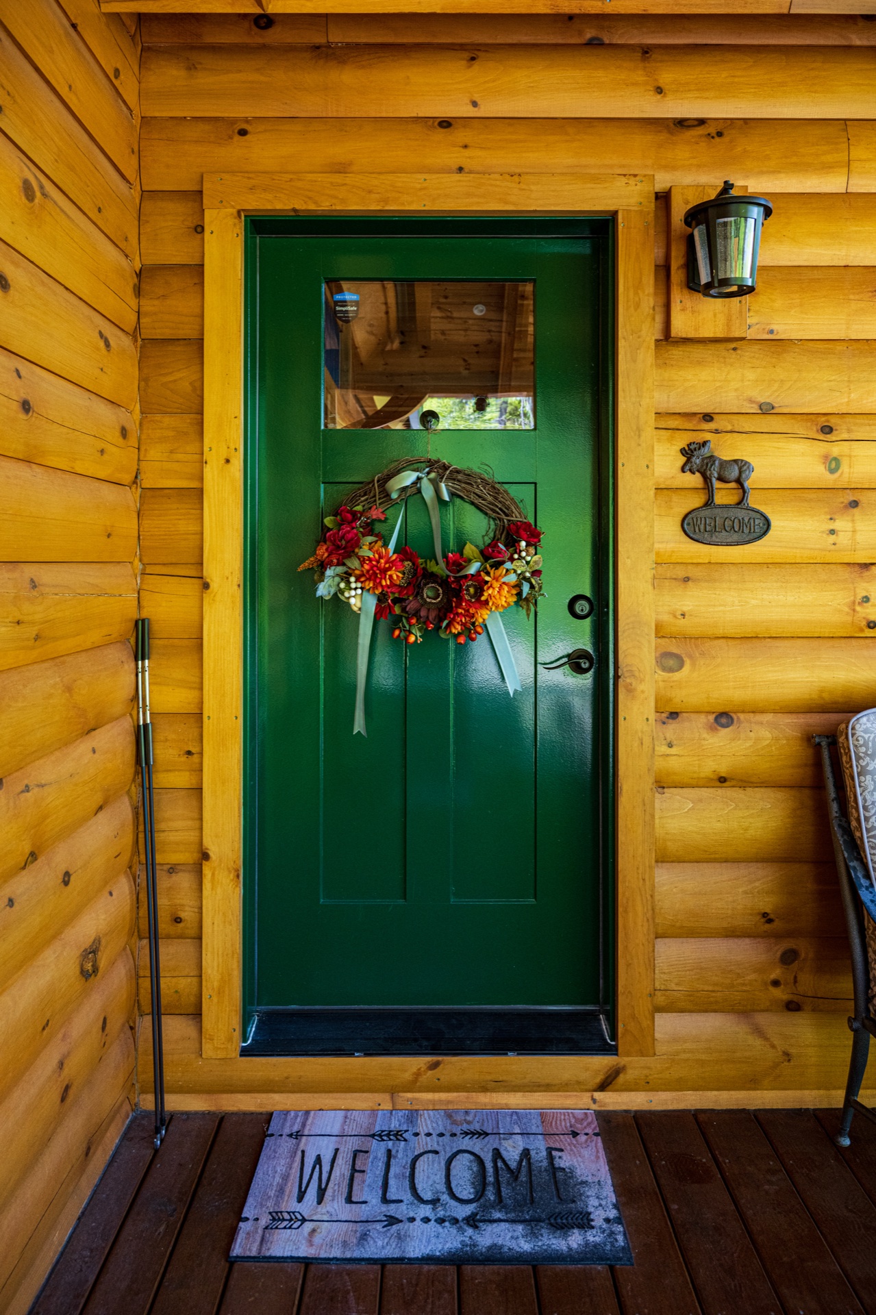 The Ossipee log home green front door with autumn wreath and welcome mat on the front porch
