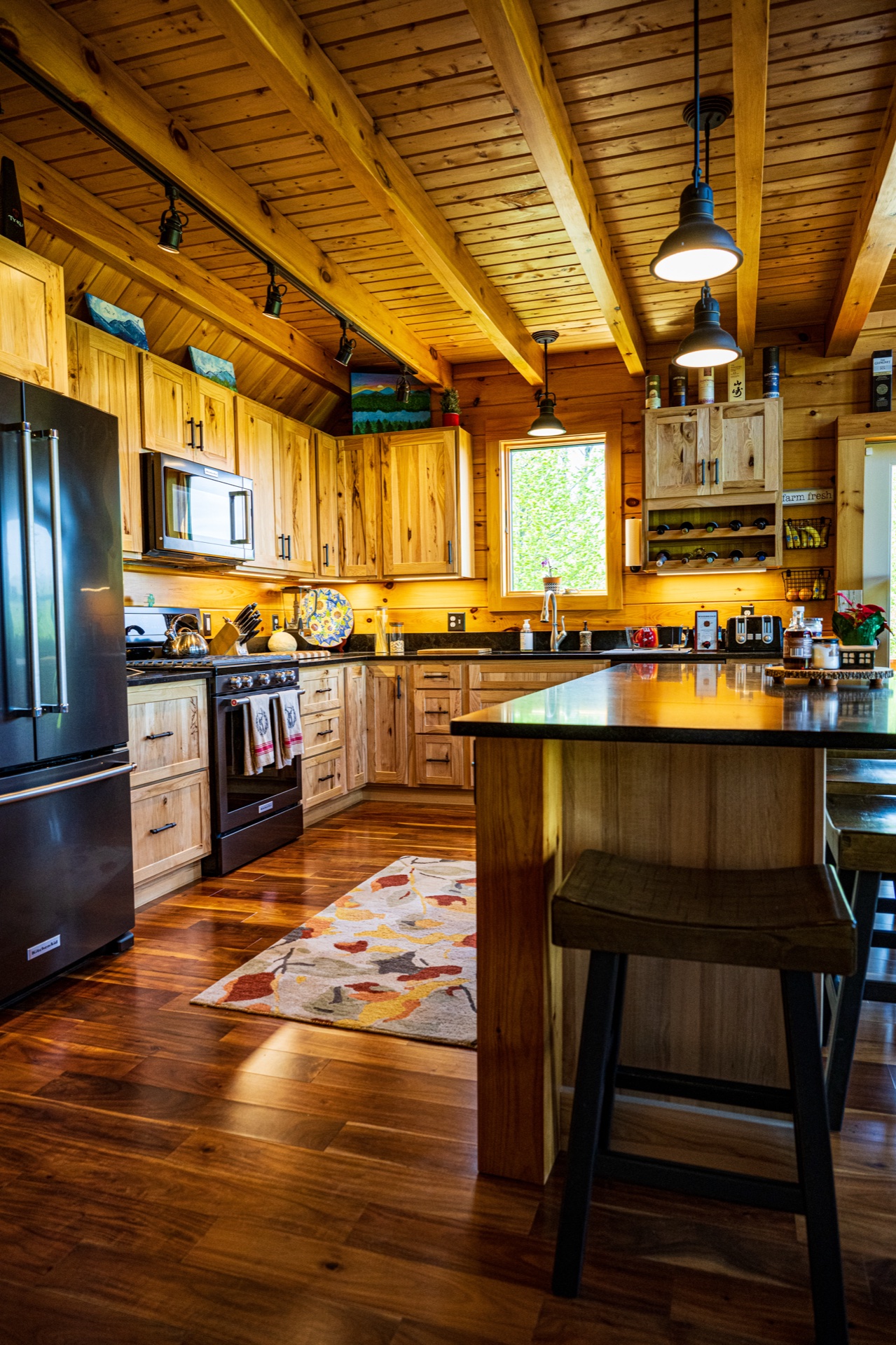 Ossipee kitchen wide view with hickory cabinets, beam ceiling, pendant lights, and dark island