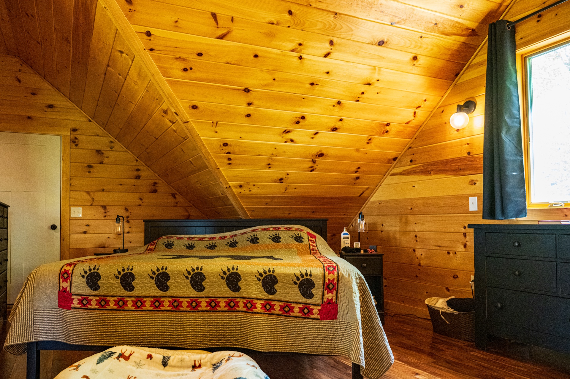 Ossipee loft bedroom with bear paw quilt and sloped pine ceiling