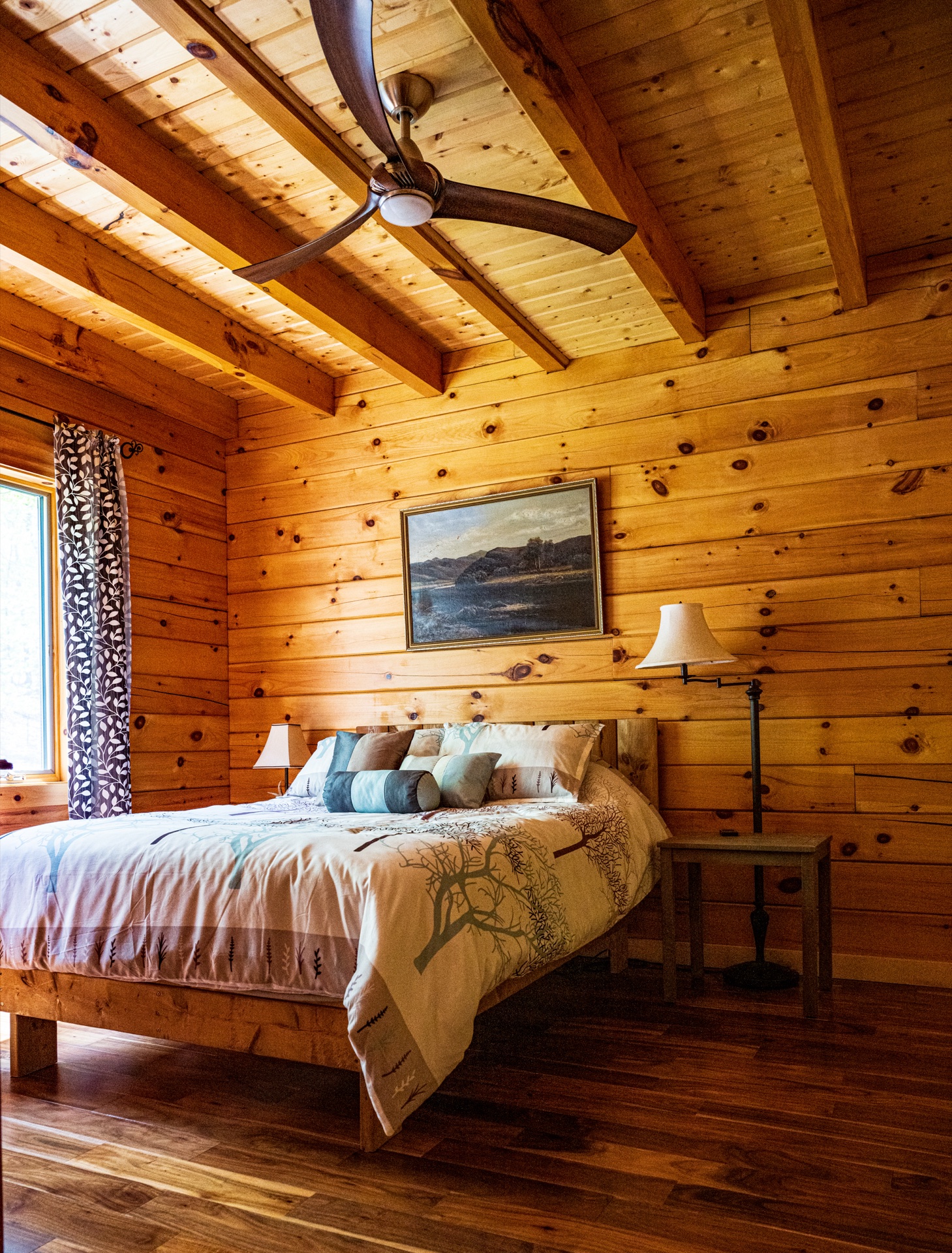 Ossipee master bedroom with ceiling fan, exposed beams, and tree-pattern bedding