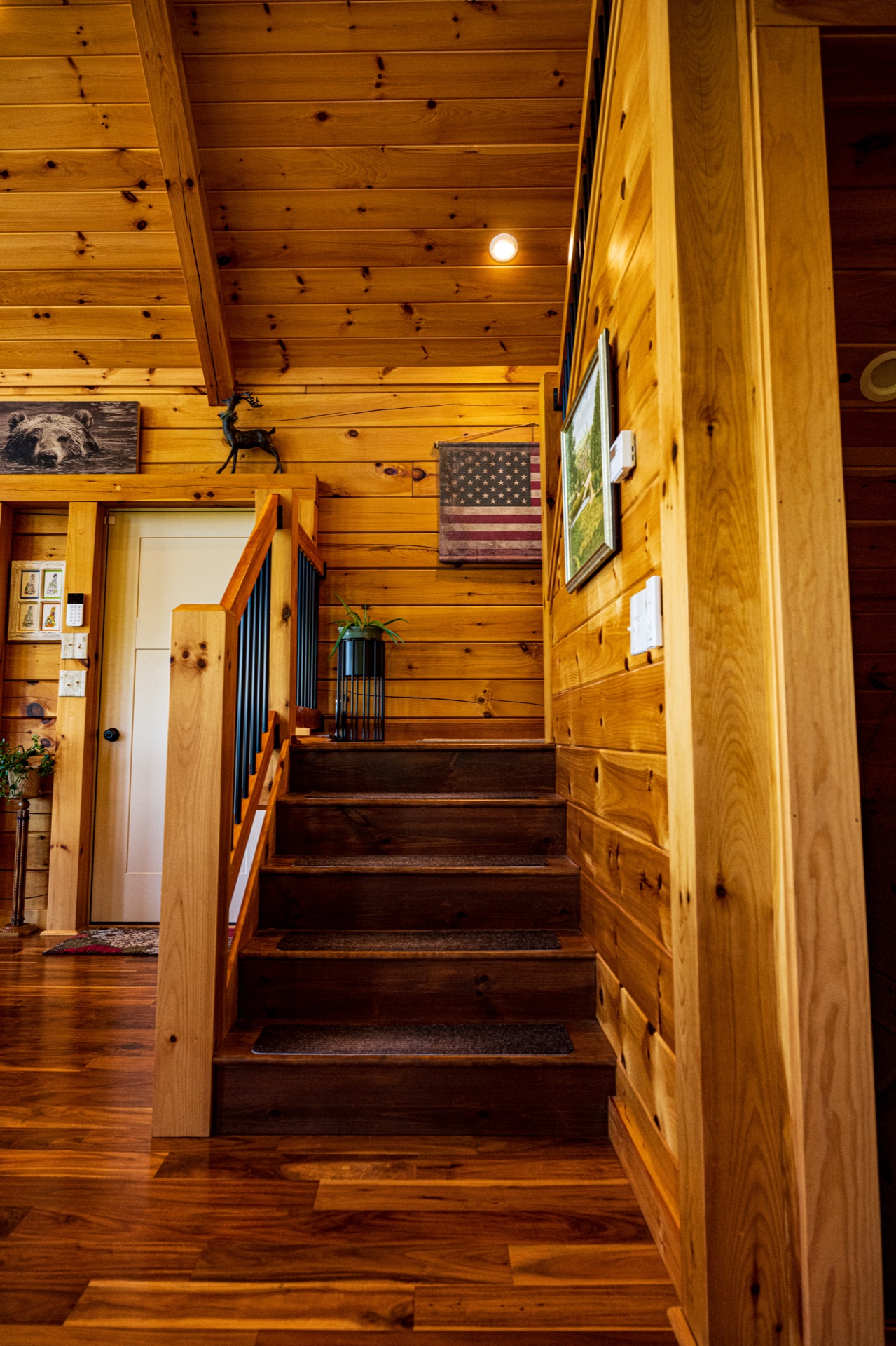 Ossipee staircase from below with hardwood treads, log walls, and American flag artwork on the wall