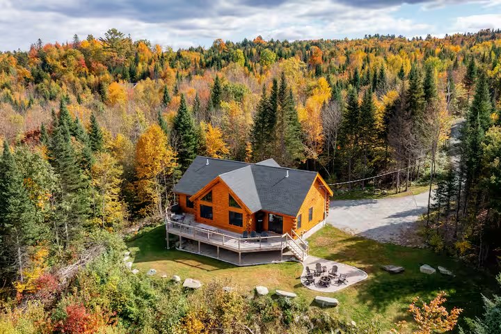 Aerial of the Sunapee log home in fall, showing the driveway approach through autumn forest