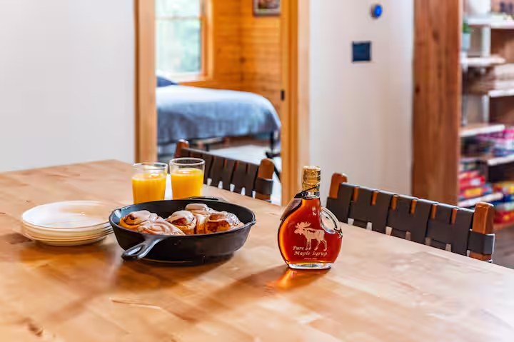 Breakfast spread of cinnamon rolls, orange juice, and pure maple syrup on the Sunapee kitchen table
