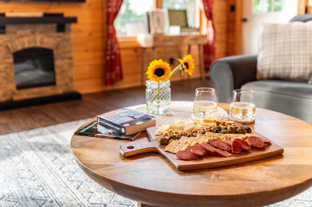 Charcuterie board with sunflowers, wine, and a White Mountain guidebook on the coffee table by the fireplace
