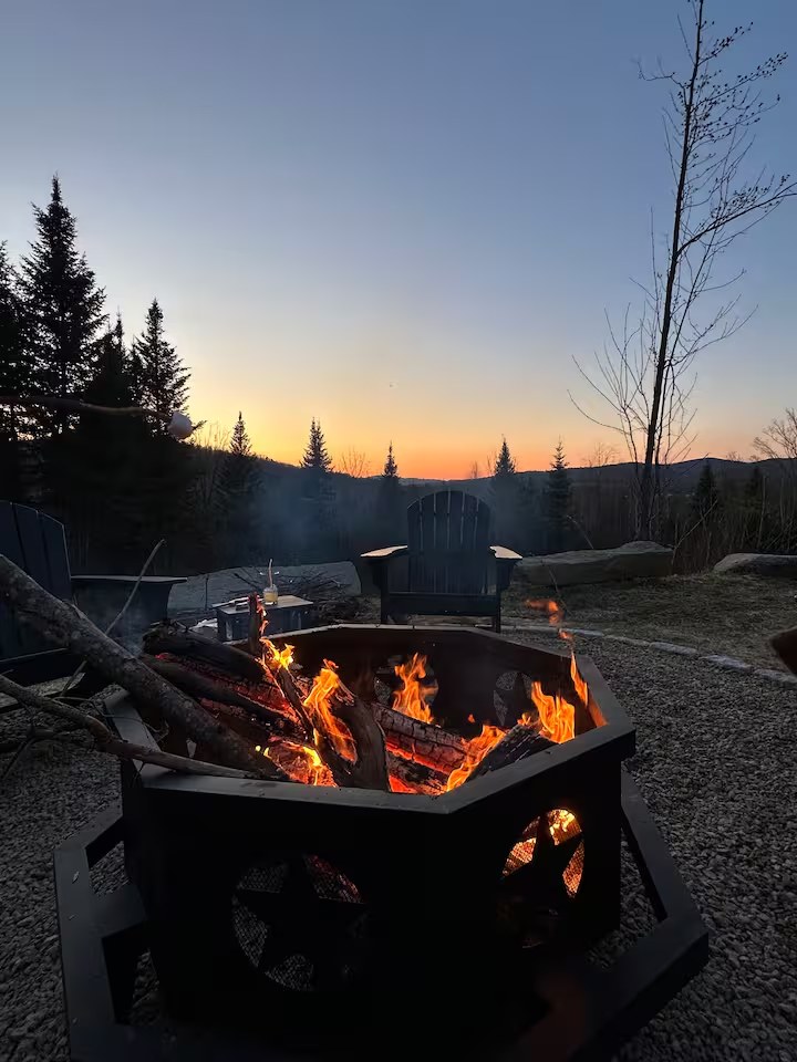 Fire pit blazing at sunset with adirondack chairs and mountain valley view from the Sunapee property