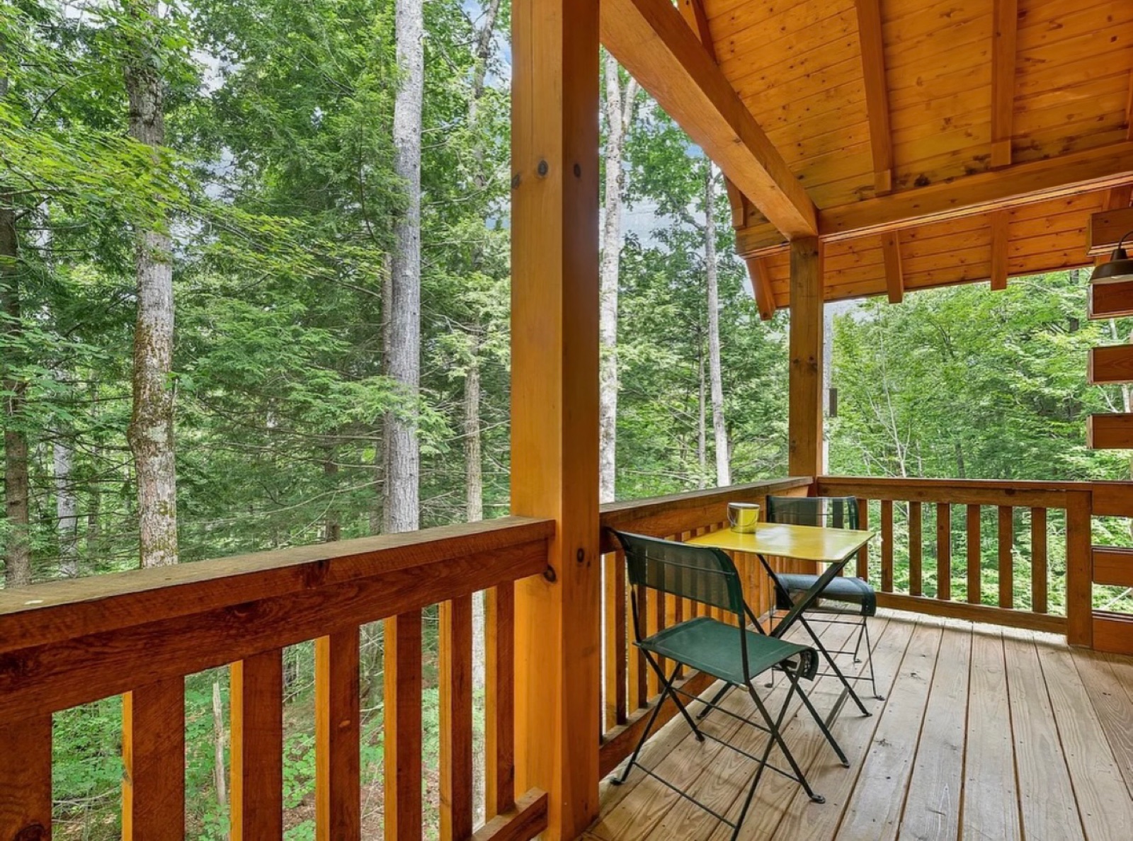 The Pine Springs tiny log home covered deck in summer with a bistro table overlooking the forest