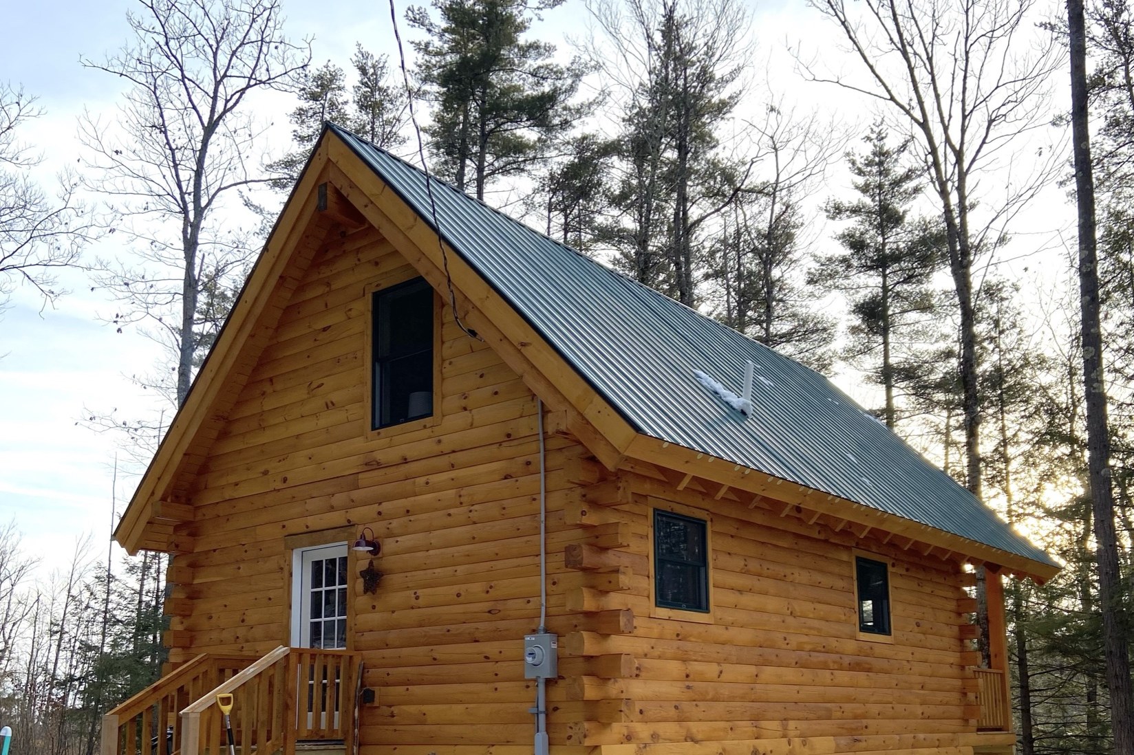 The Pine Springs tiny log home front exterior in winter with snow and metal roof