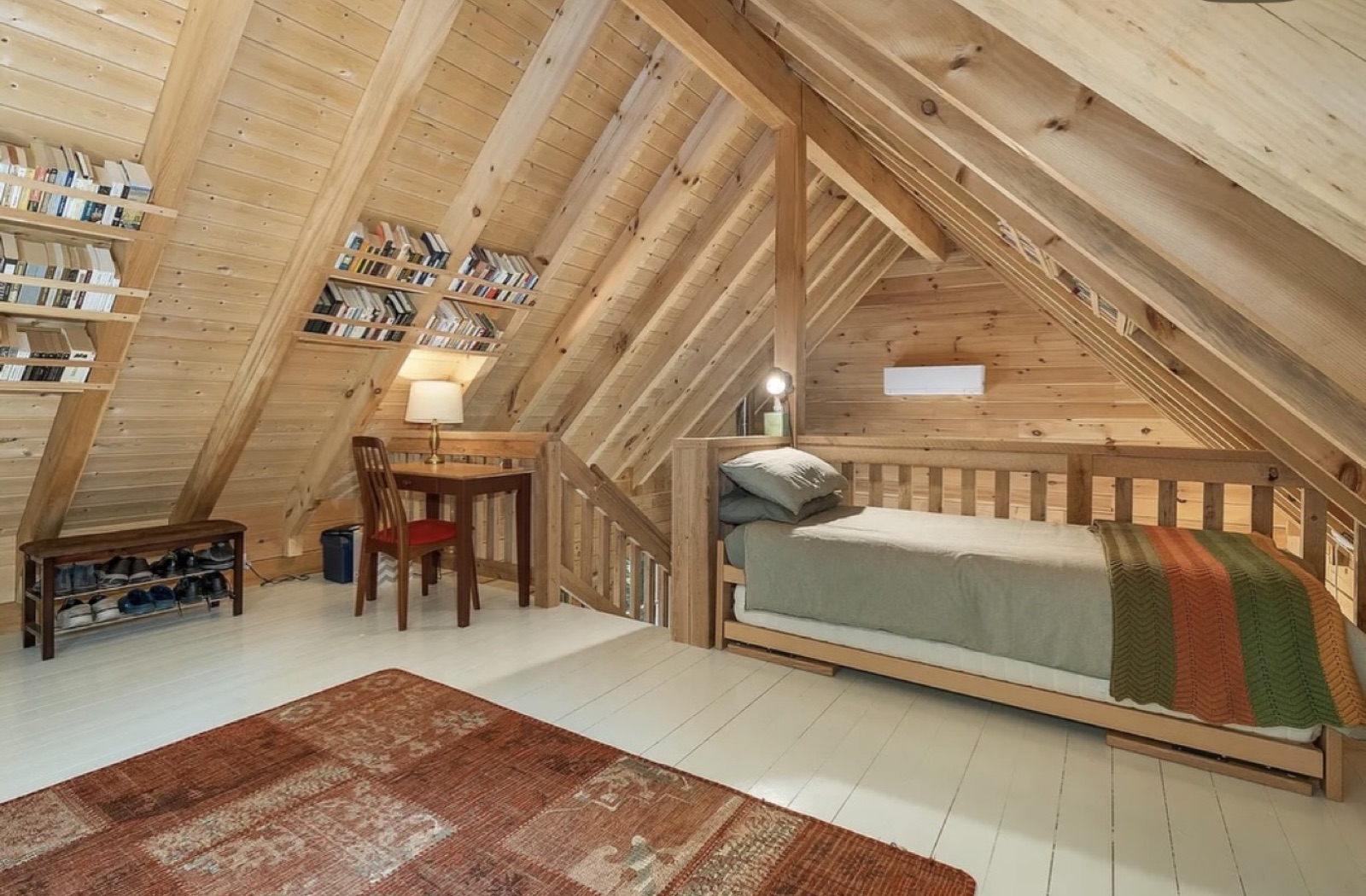 A loft bedroom inside the Pine Springs tiny log home with a daybed, desk, and bookshelves