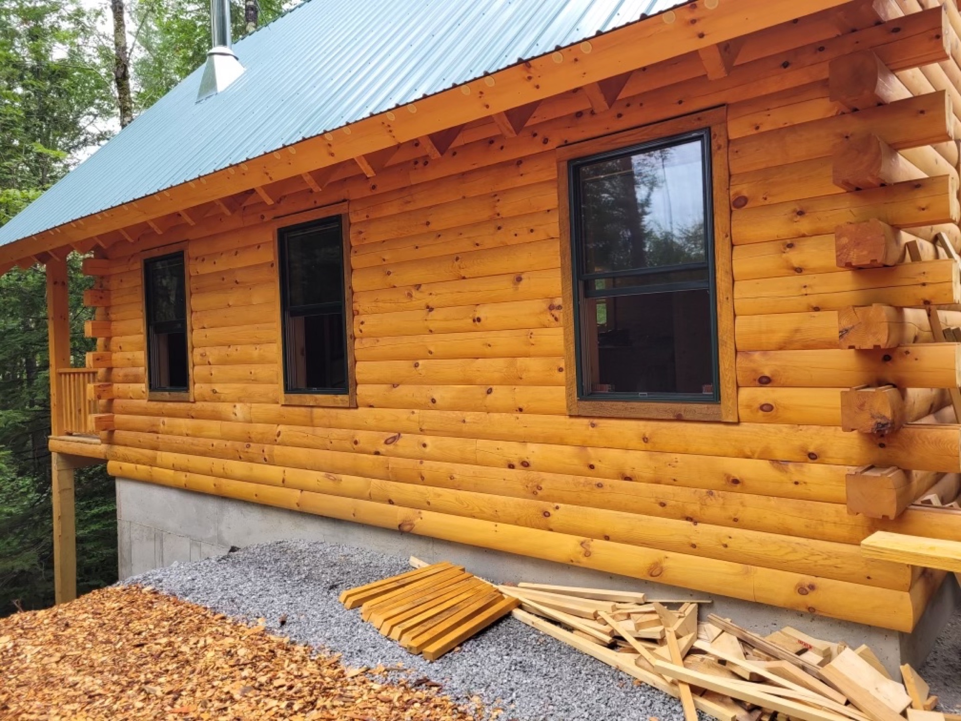 The Pine Springs tiny log home side view in summer showing log siding wall and windows