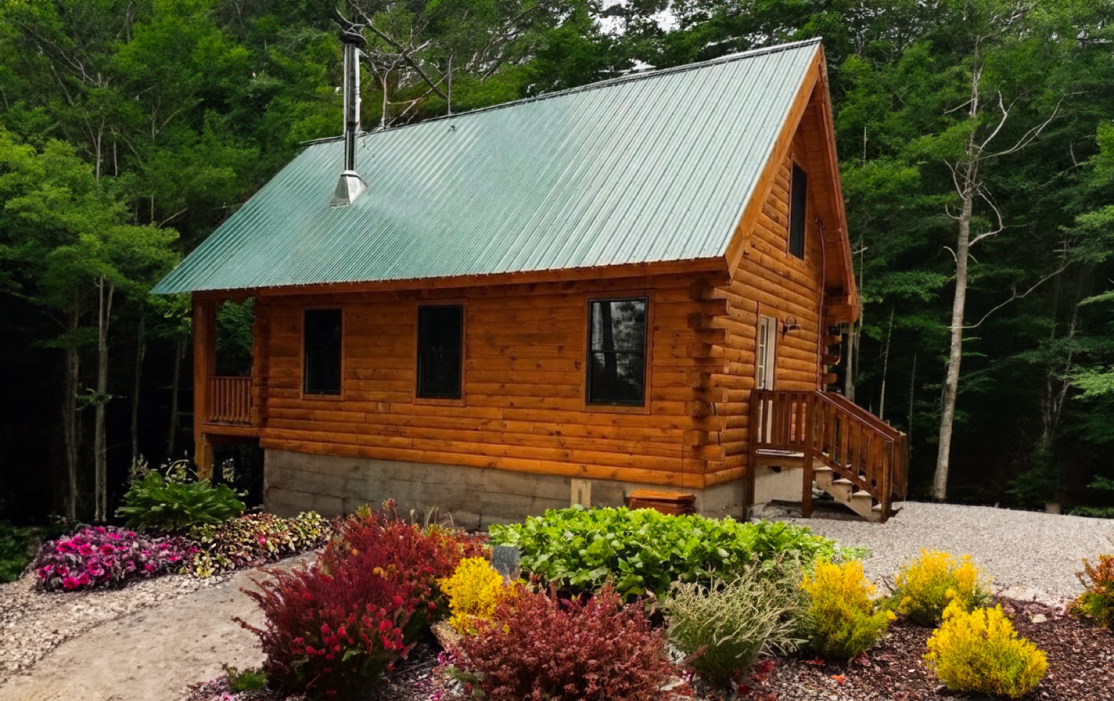 The Pine Springs tiny log home in summer with a landscaped flower garden, green metal roof, and Eastern White Pine log siding