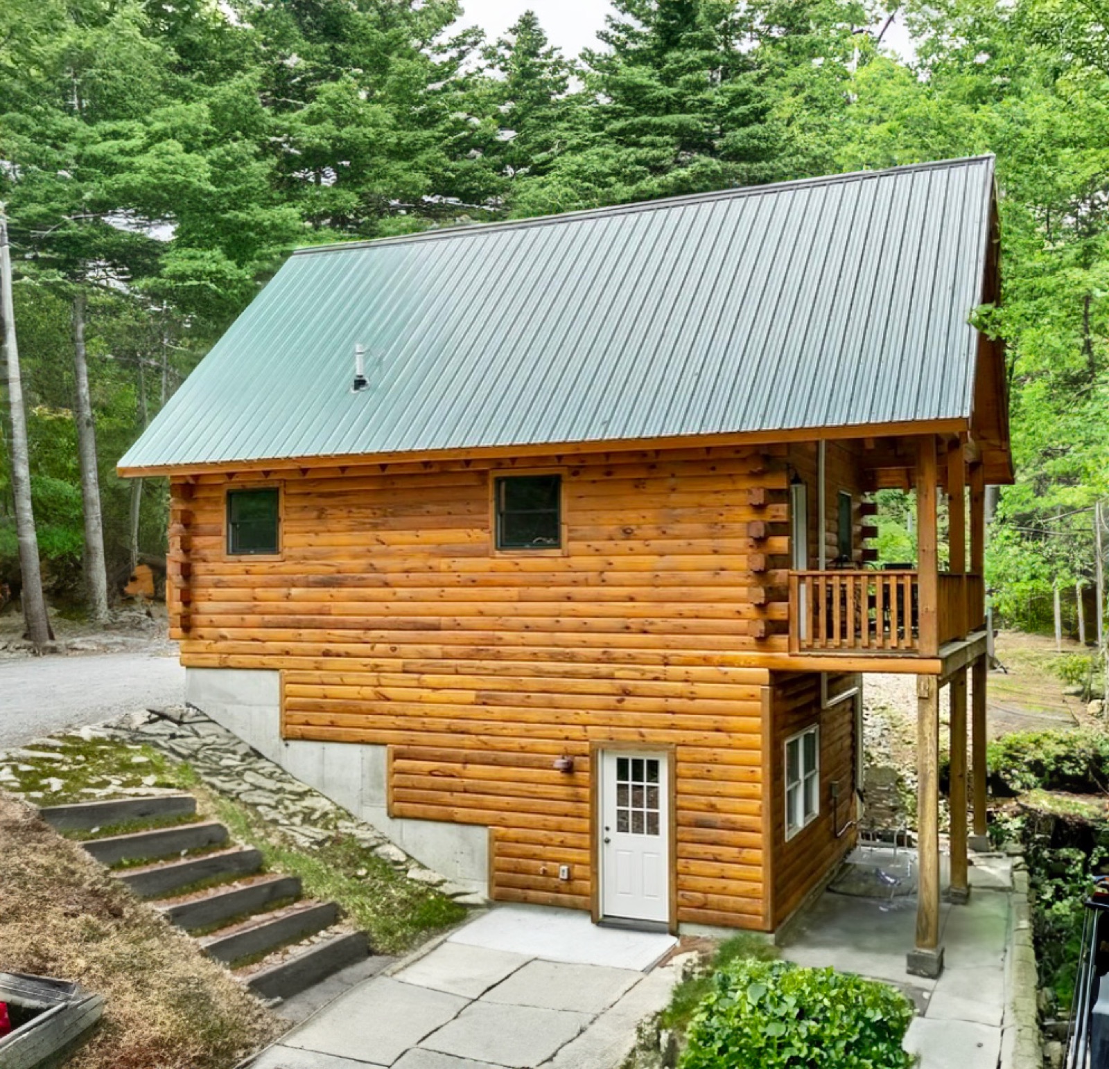 The Pine Springs tiny log home side exterior in summer with a green metal roof and covered porch
