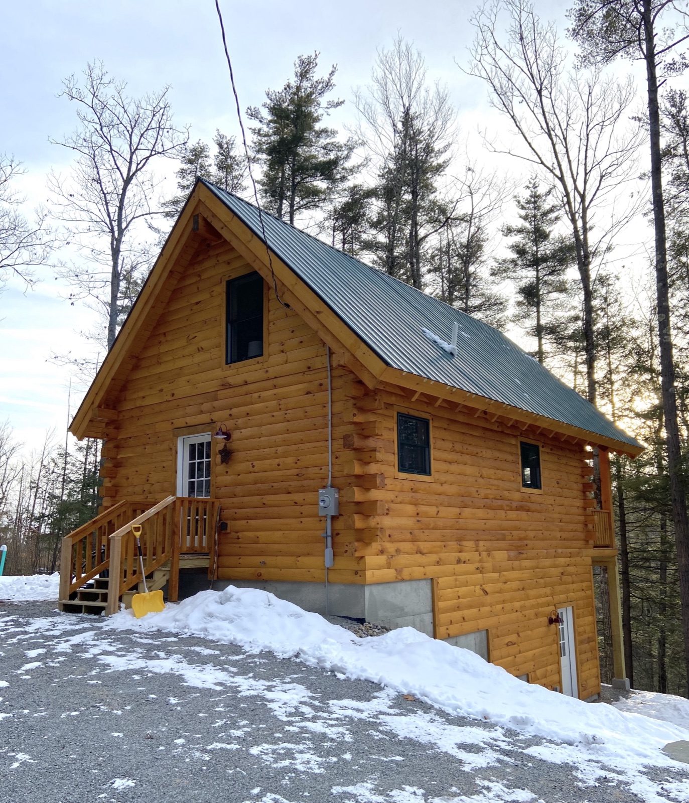 The Pine Springs tiny log home exterior in winter with snow, a metal roof, and log siding