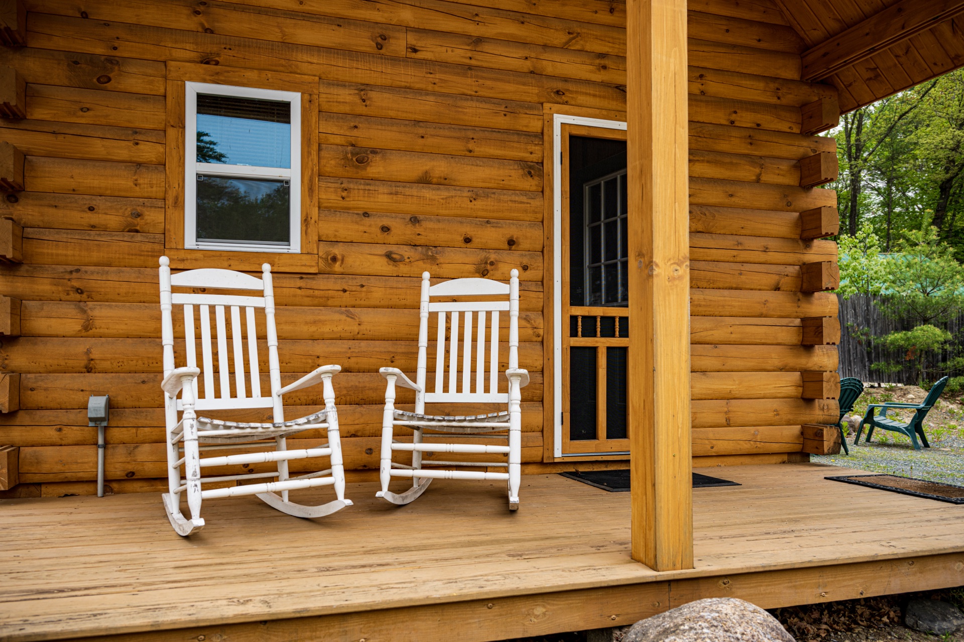 Tiny log home front porch with white rocking chairs and screen door