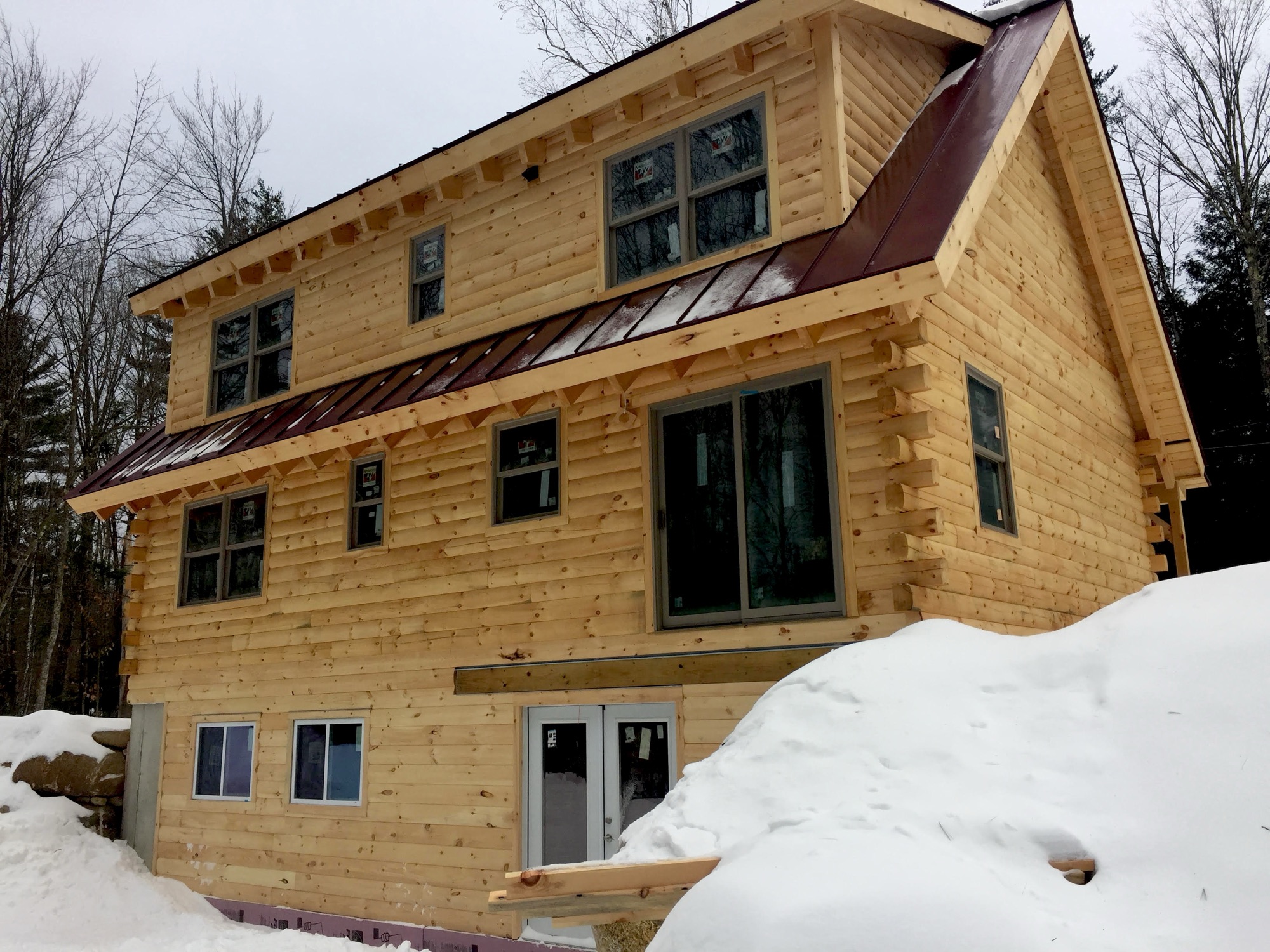 The Winnisquam log home showing its Eastern White Pine log siding, dormers, and standing-seam metal roof accents